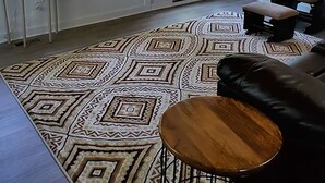Ein Wohnzimmer mit Teppichmuster, einer Ledersofa, einem Holztisch, einer Lampe und einer Uhr an der Wand.
