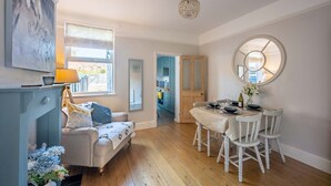 A cozy living room with a sofa, a dining table set for four, and a large mirror. - Swift Host | Central | 3 Bedrooms | Parking (Norwich)