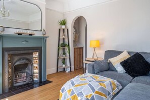 Ein Wohnzimmer mit Kamin, einer Couch, einer Lampe und einem Pflanzenregal.