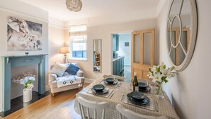 A dining area with a table set for four, a sofa, a fireplace, and a large mirror. - Swift Host | Central | 3 Bedrooms | Parking (Norwich)