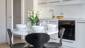 A modern kitchen with white cabinets, a black dining table with white bowls and glasses, and a vase of white flowers. - Swift Host | Park Lane | 2 Bed | Great Location (Norwich)