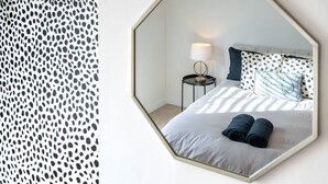 A bedroom with a bed, a nightstand, a lamp, and a mirror. - Swift Host | Stylish City Terrace | Parking (Norwich)