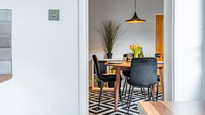 A modern dining area with a wooden table, black chairs, and a hanging pendant light. - Swift Host | Stylish City Terrace | Parking (Norwich)