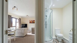 A modern hotel room with a glass-enclosed shower, a white toilet, a sofa, and a TV in the living area. - Swift Host | Fishergate 2 bed | River View (Norwich)