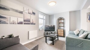 A modern living room with a grey sofa, a television, a coffee table, and a bookshelf. - Swift Host | 2 beds | Central Location | Cowgate (Norwich)