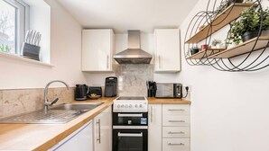 A compact kitchen with a sink, stove, microwave, and cabinets. - Swift Host | 2 beds | Central Location | Cowgate (Norwich)