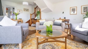 A modern living room with grey sofas, a round coffee table, and a staircase leading to an upper level.