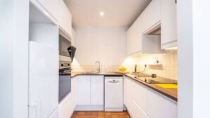 A compact kitchen with white cabinets, a tiled backsplash, and a tiled floor.