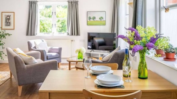 A modern living room with a dining table set for two, a sofa, a TV, and a window with curtains.