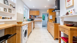 Une cuisine moderne avec des meubles en bois, un lave-linge encastré et une grande fenêtre qui laisse entrer la lumière naturelle.