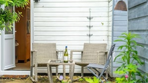 Une terrasse avec des meubles en osier, une bouteille de vin et des verres.
