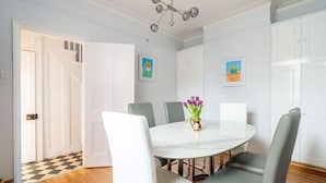 Une salle à manger avec une table ronde, des chaises recouvertes d’un tissu gris et un vase rempli de fleurs violettes.
