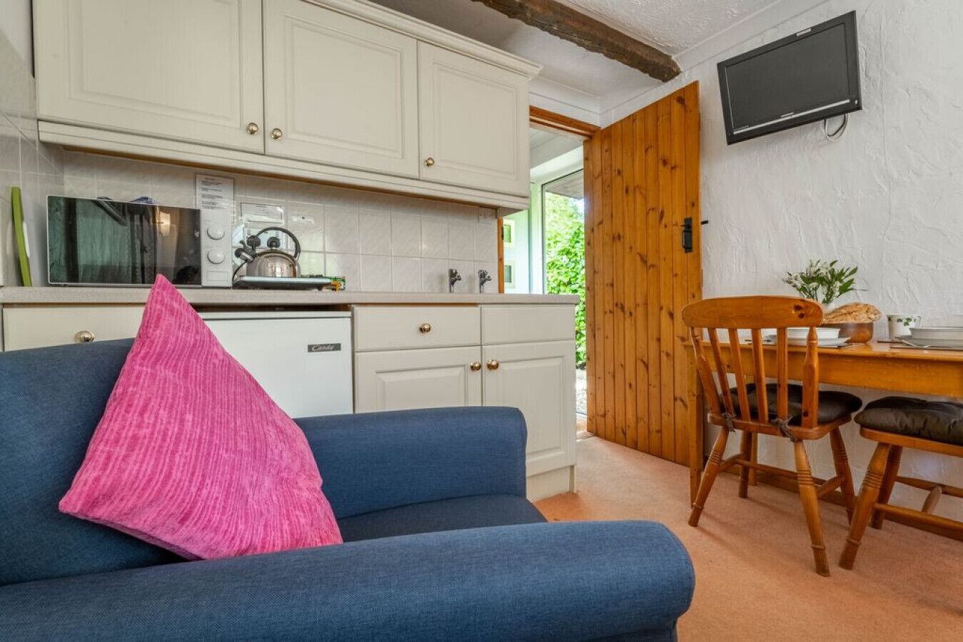 A cozy room with a blue sofa, a wooden dining table, and a kitchen area with white cabinets and a microwave.