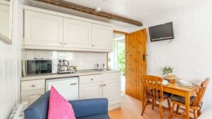 A compact kitchen with white cabinets, a microwave, and a kettle. There's a dining area with a wooden table and chairs, and a TV mounted on the wall. - Swift Host The Nook Rural Barn near the Norfolk Broads (Norfolk Broads)