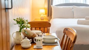 A hotel room with a neatly made bed, a bedside table with a lamp, a vase with flowers, and a wooden chair. - Swift Host The Nook Rural Barn near the Norfolk Broads (Norfolk Broads)