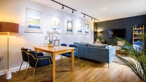 Ein modernes Wohnzimmer mit einem Holzesstisch, blauen Stühlen, einem grauen Sofa und einem an der Wand befestigten Fernseher.