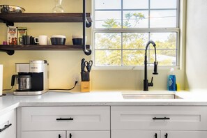 A kitchen with a coffee maker, a sink, and a window with a view of trees.