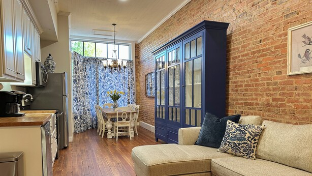 A cozy kitchen with wooden flooring, a dining area with a table and chairs, and a blue cabinet against a brick wall. - Charming 2 BR/2 bath in Historic District - Rent 1 Suite or Both/8-16 people! (Troy)