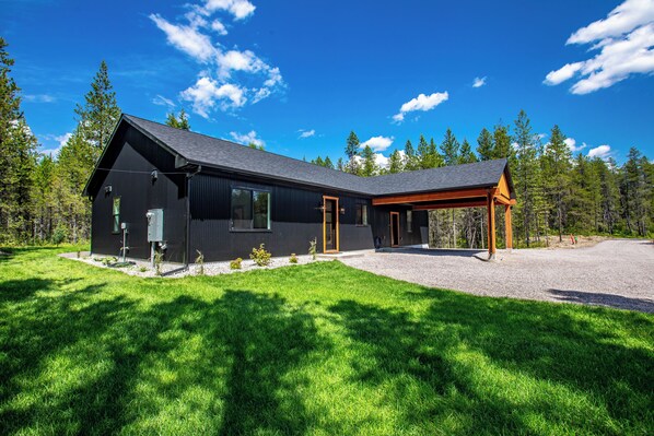 A modern house with a large porch, surrounded by a well-maintained lawn and tall trees.