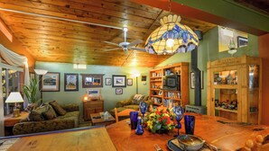 A cozy living room with a wooden ceiling, a dining table set with blue glassware, and a bookshelf filled with books and decorative items. - Raven's Grotto (Flagstaff)