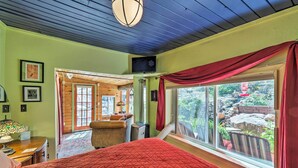 A bedroom with a large bed, a television, a desk with a lamp, and a window with curtains. - Raven's Grotto (Flagstaff)