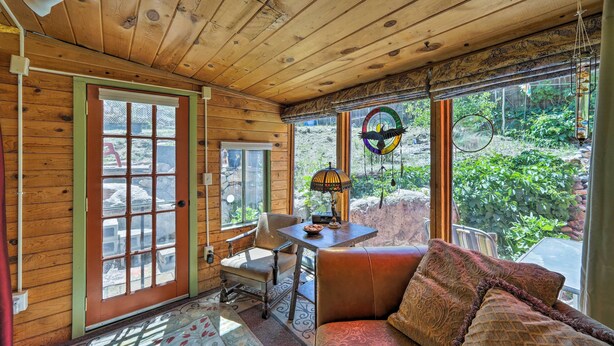 A cozy cabin interior with wooden walls, a large window, a cushioned bench, and a table with a lamp. - Raven's Grotto (Flagstaff)