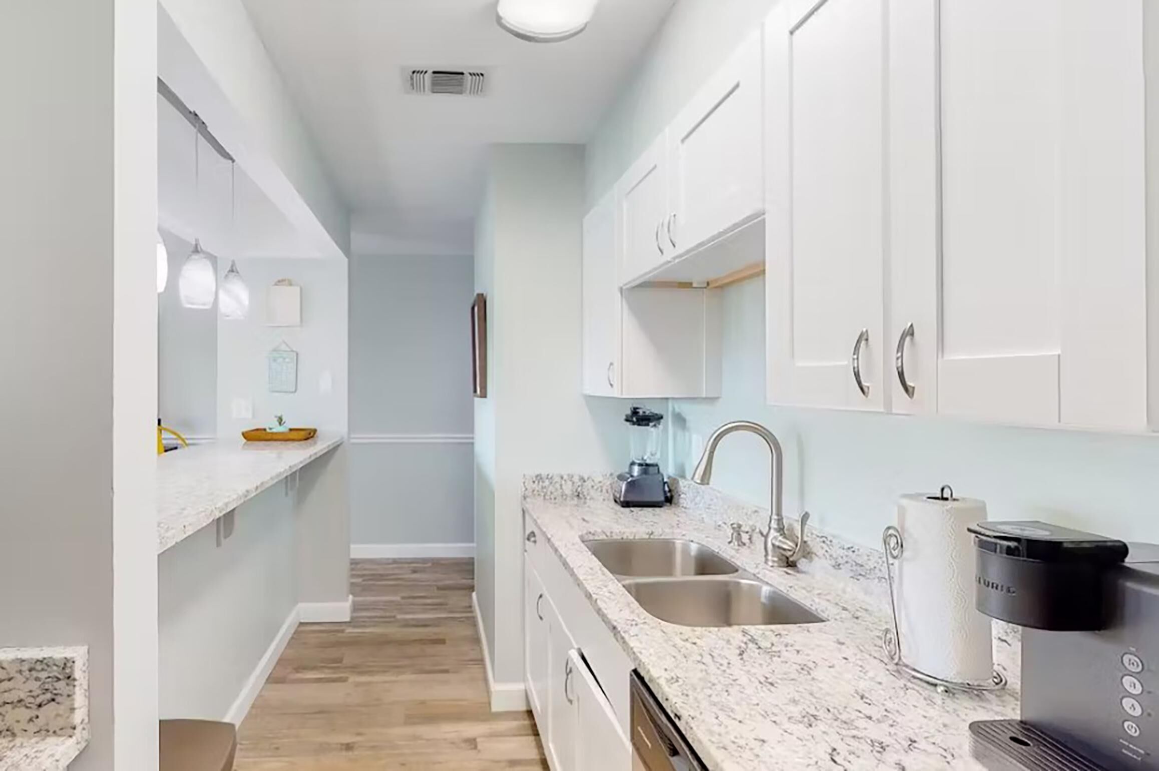 A modern kitchen with white cabinets, granite countertops, and a coffee maker.