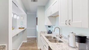 A modern kitchen with white cabinets, granite countertops, and a coffee maker. - Endless Summer D5 (Panama City Beach)