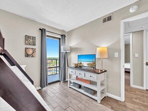 A hotel room with a balcony, a TV, a lamp, and a bed. - Edgewater Tower 3-1110 - South of Heaven (Panama City Beach)