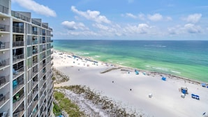Ein Hochhaus-Hotel mit mehreren Balkonen mit Blick auf einen Strand mit klarem türkisblauem Wasser und weißem Sand.