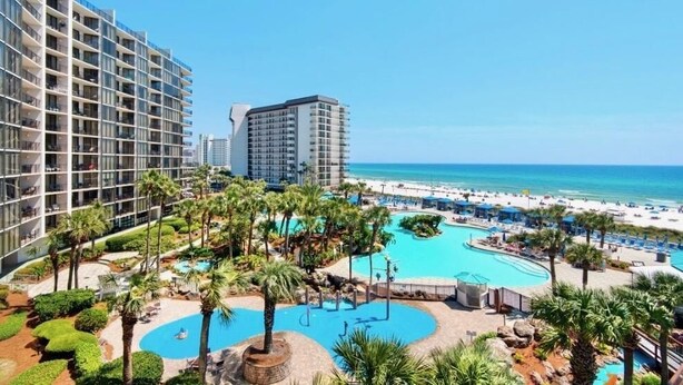 Ein Hotel mit großzügiger Poolanlage, Palmen und Blick auf den Strand.