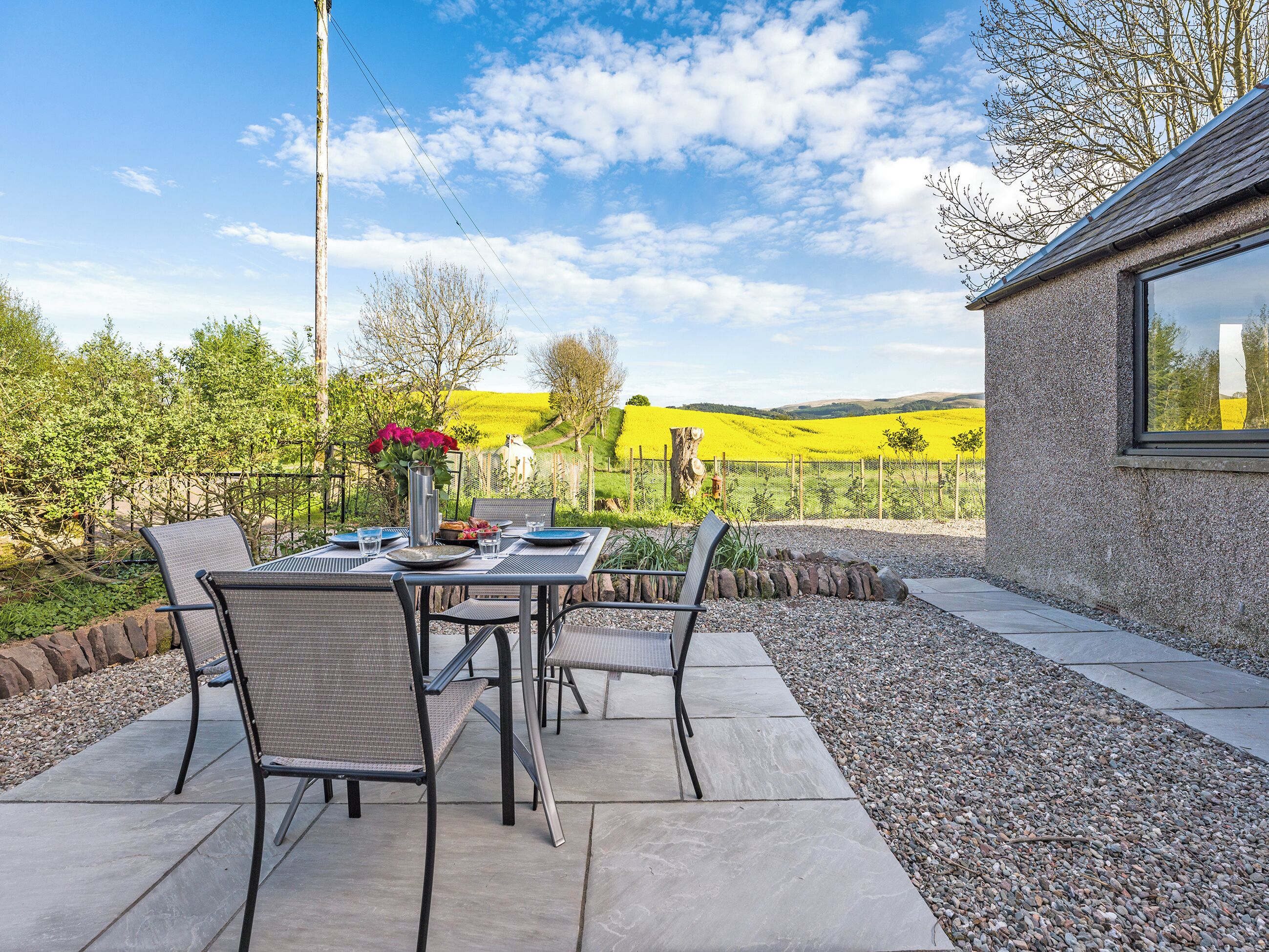 An outdoor dining area with a table set for two, surrounded by chairs, and a view of a vineyard in the background.
