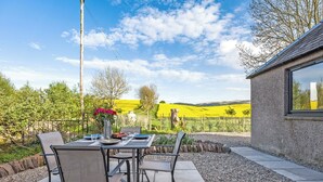 Un espace de restauration en plein air avec une table dressée pour deux personnes, entourée de chaises, et une vue sur un vignoble en arrière-plan.