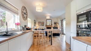 Une cuisine moderne avec un plancher en bois, un coin repas avec des chaises en bois, une grande horloge et un four encastré.