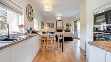 A modern kitchen with wooden flooring, a dining area with wooden chairs, a large clock, and a built-in oven.