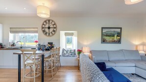 Une cuisine moderne avec un coin repas, une grande horloge et un salon confortable avec un canapé et un tableau.