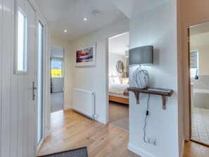 A modern bedroom with a bed, a bedside table with a lamp, a wall-mounted TV, and a radiator. - Newbigging Farm Cottage (Auchterarder)