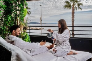 A couple in white bathrobes sitting on a bed with a view of the sea and palm trees. - [2] Blue Summer Vibes Mini Studio, A/C, parking, 50m from beach, SPA access (La Ciotat)