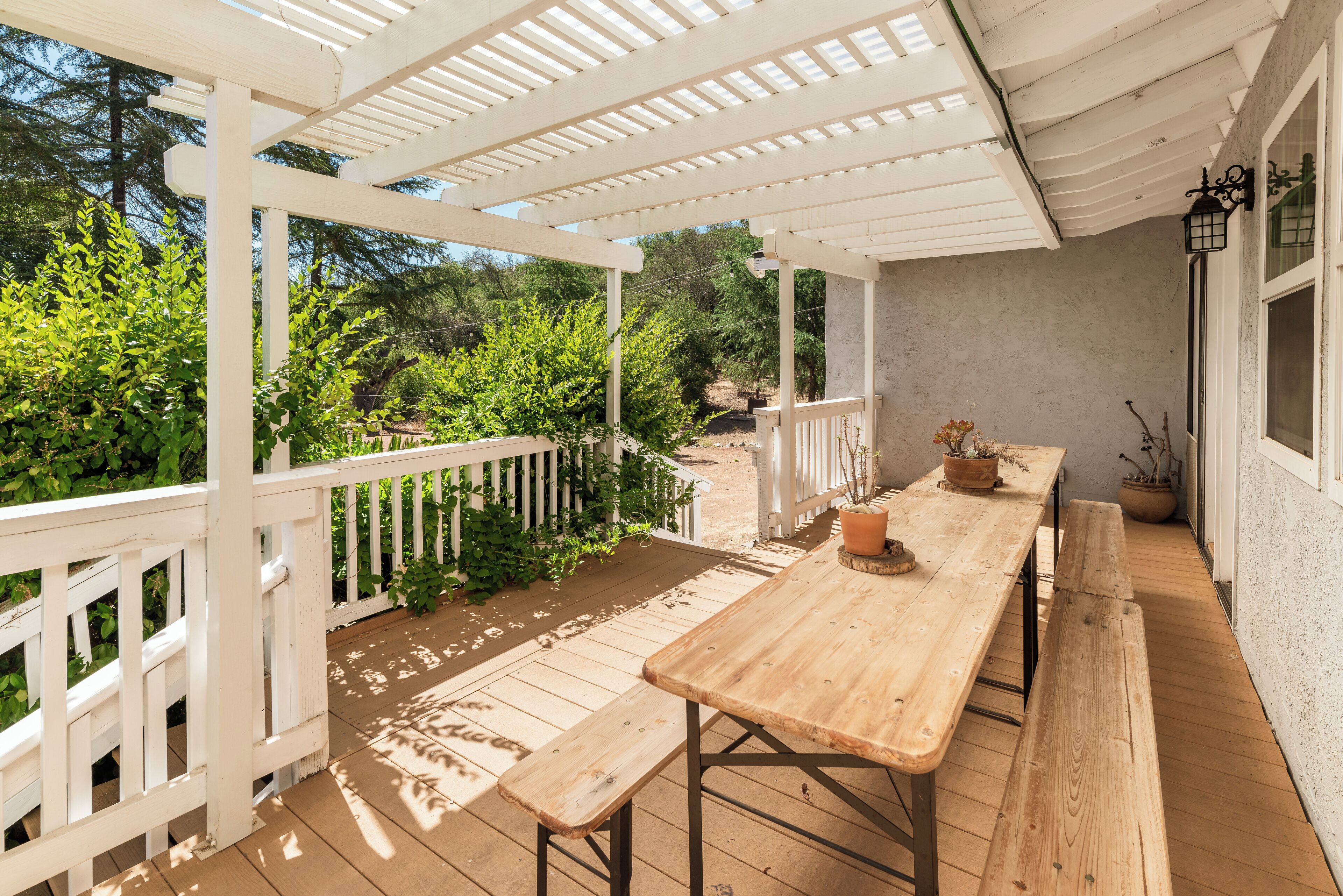 A wooden deck with a white railing, a wooden table with benches, and potted plants.