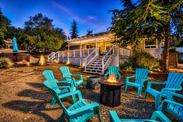 A patio area with outdoor seating and a fire pit, surrounded by trees and a building with a deck.