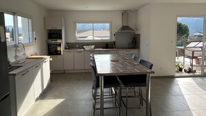 A modern kitchen with a dining area, large windows, and a view of the mountains.