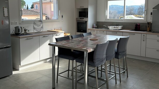 A modern kitchen with a dining area, featuring a large island with chairs, a built-in oven, and a microwave.