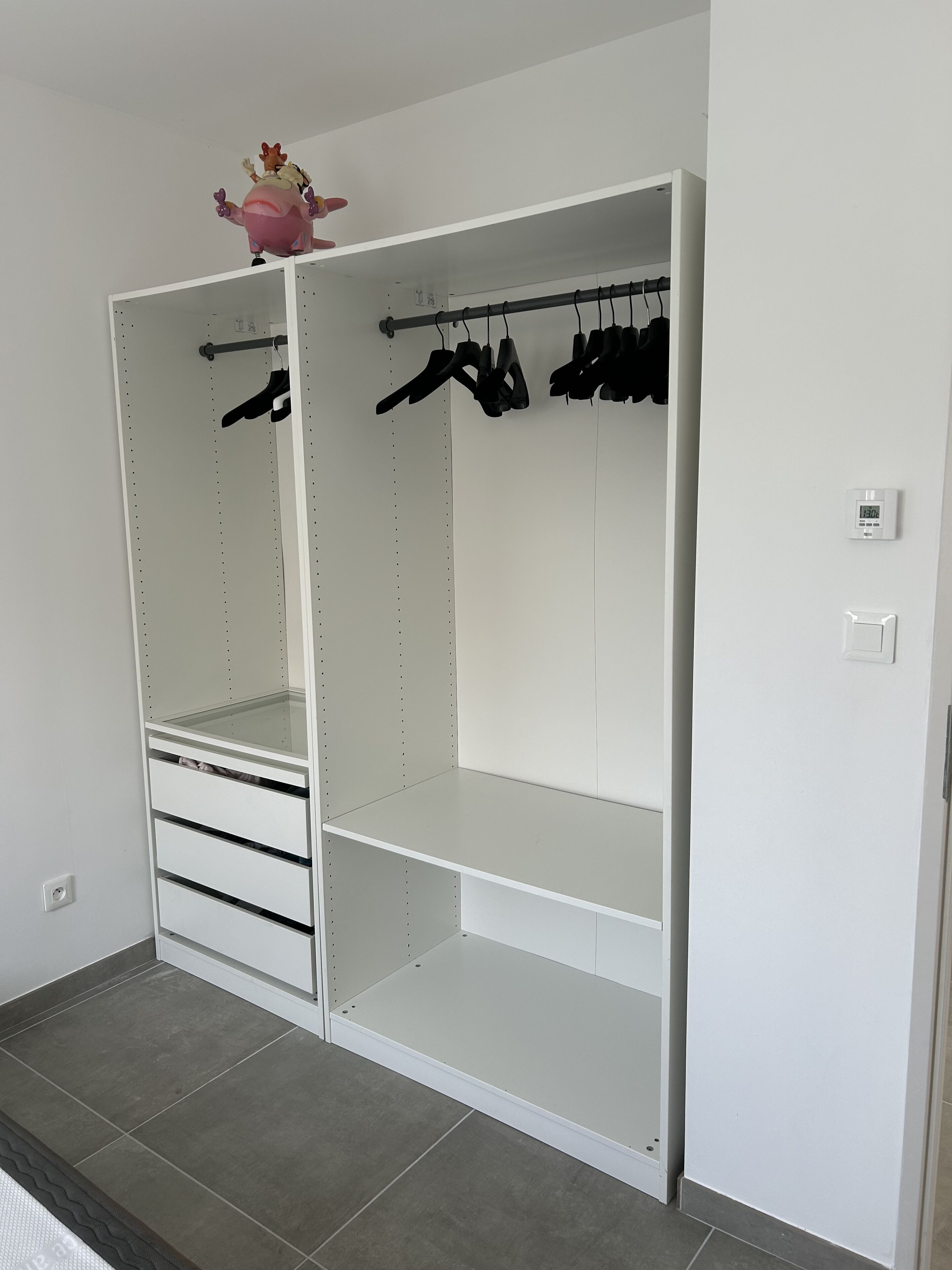 Un dressing blanc, ouvert, avec des étagères, une tringle pour suspendre les vêtements et des tiroirs.