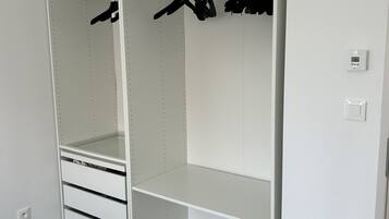 Un dressing blanc, ouvert, avec des étagères, une tringle pour suspendre les vêtements et des tiroirs.