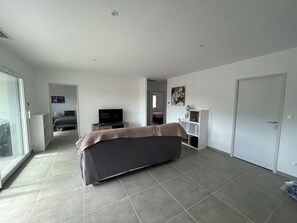 Relax in this spacious living room with a large sofa, flat-screen TV, and sliding glass door leading to an outdoor area.