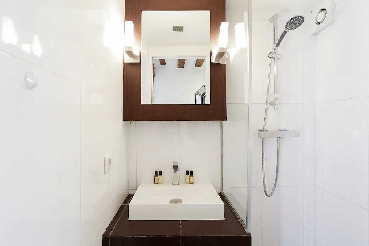 A bathroom with a white sink, two bottles of toiletries, a mirror with a wooden frame, and a shower with a handheld showerhead.