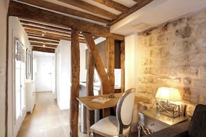 A narrow hallway with exposed wooden beams, a stone wall, and a table with a lamp.