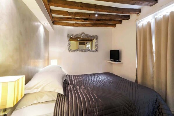 A bedroom with a bed, a bedside lamp, a TV, and a mirror on the wall.