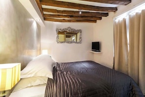 A bedroom with a bed, a bedside lamp, a TV, and a mirror on the wall.