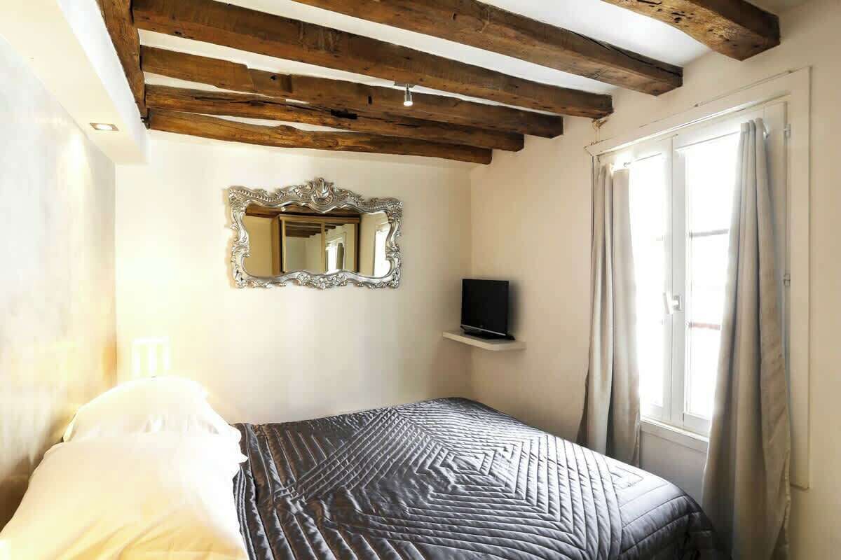 Une chambre à coucher avec un lit, un miroir, une télévision et une fenêtre avec des rideaux.